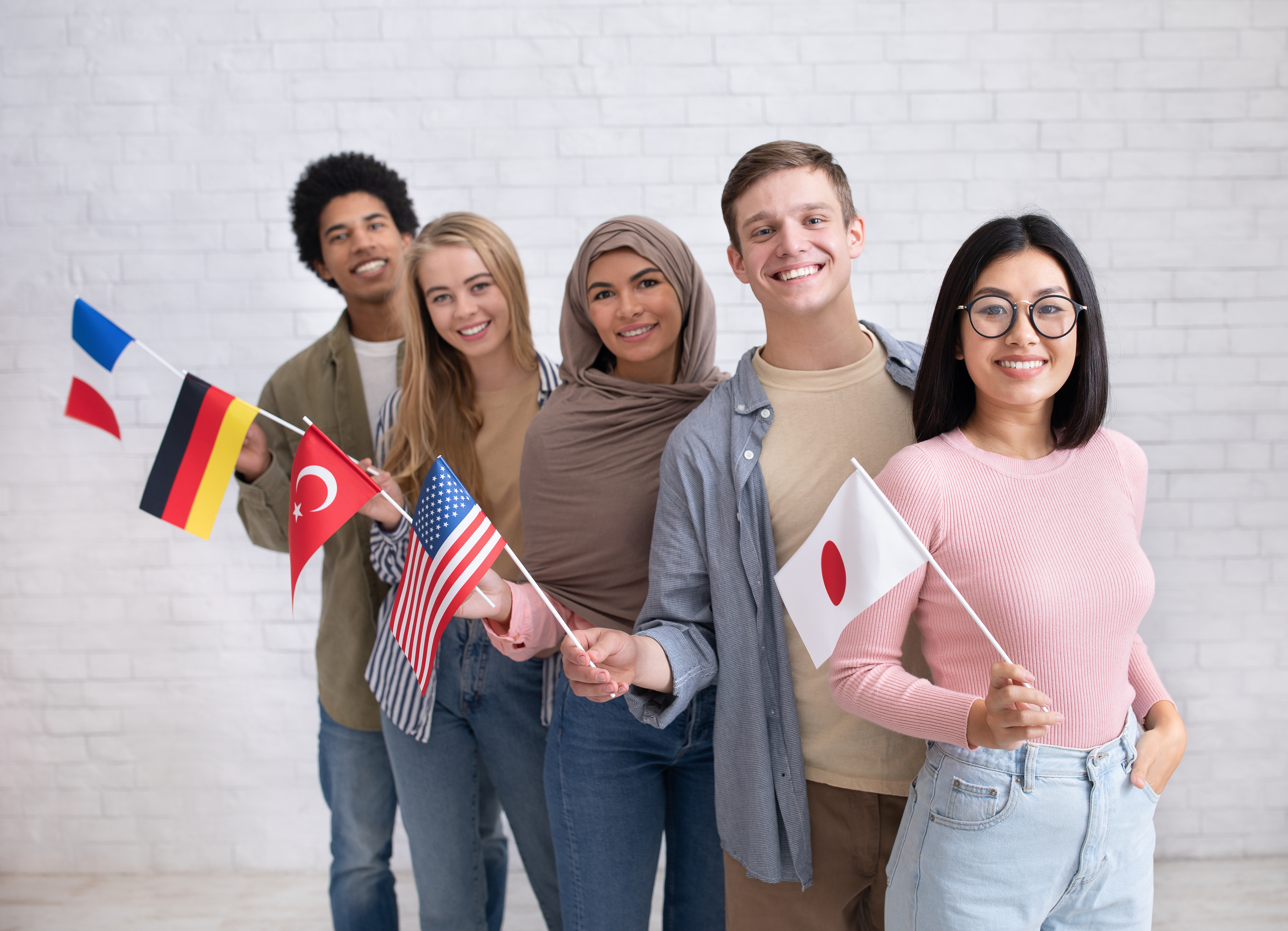 Exchange students and language school for different people. Funny digital young international pupils holding flags of USA, Japan, Turkey, Germany and France in classroom, studio shot, empty space